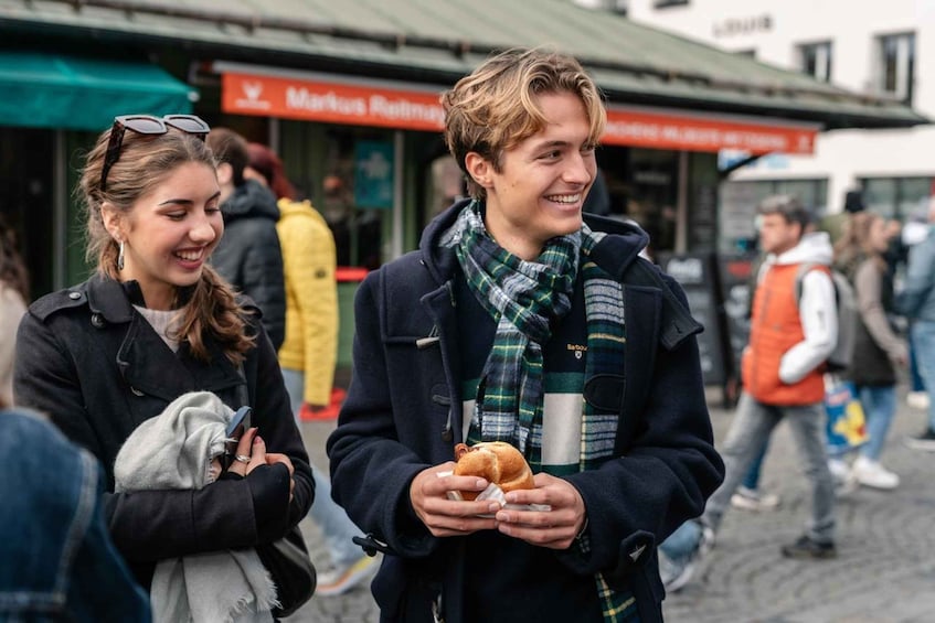 Two people holding a sandwich, with a building labeled 'Markus Riesen' in the background. 5