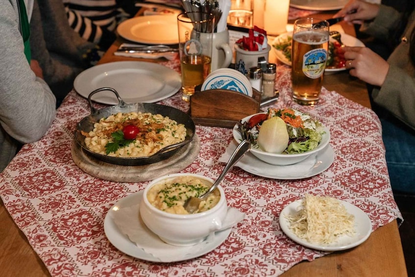A table with a variety of dishes, including a bowl of pasta, a bowl of soup, and a plate of salad, along with a glass of beer. 4