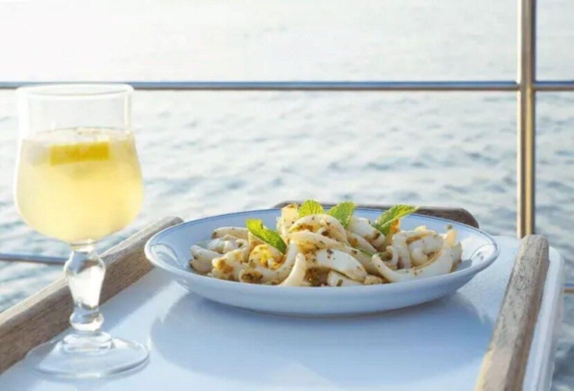 A plate of pasta with a lemon wedge and mint garnish, accompanied by a glass of white wine on a wooden tray. 3