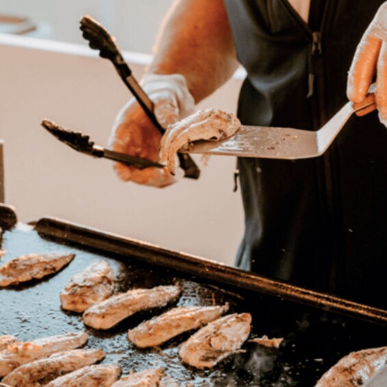 A person grilling chicken on a flat griddle. 1