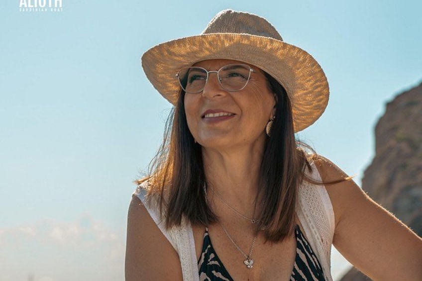 Una persona con un cappello di paglia e una collana, in piedi all'aperto con un cielo sereno sullo sfondo. 2