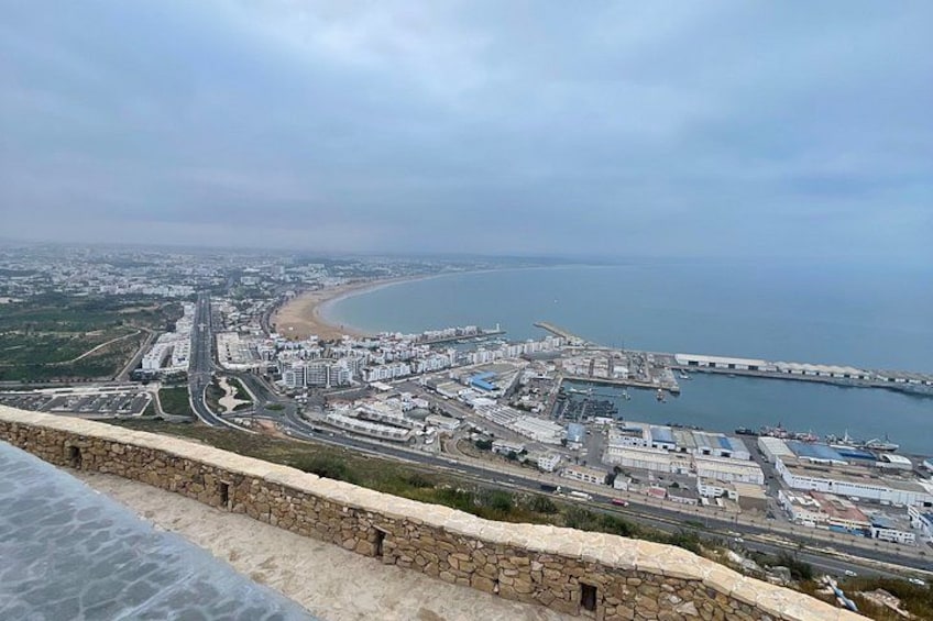 Paesaggio costiero con una spiaggia ampia, un porto turistico e un muro di pietra. 2