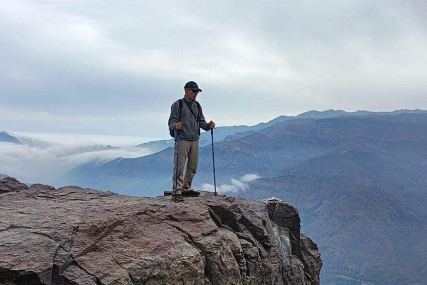 Una persona in piedi su una roccia sporgente, con una catena montuosa sullo sfondo. 5