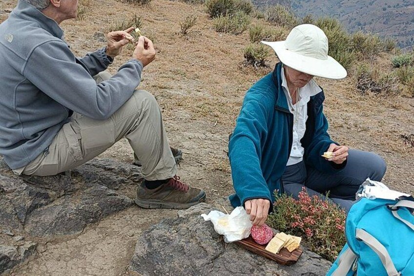 Due persone sedute su una superficie rocciosa all'aperto, una con uno spuntino e l'altra che osserva qualcosa. 3