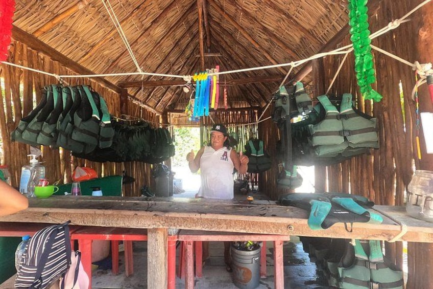 A person standing in a hut with life jackets hanging on the walls and a table with various items. 3