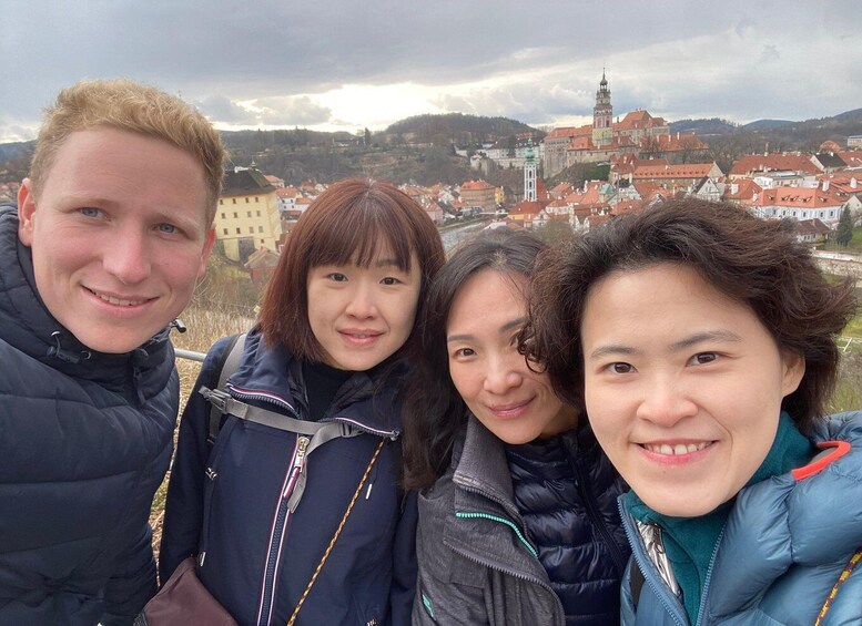 Four people standing outdoors with a historic town and a prominent tower in the background. 3