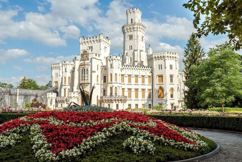 A castle with multiple towers and a well-manicured garden with red and white flowers. 1