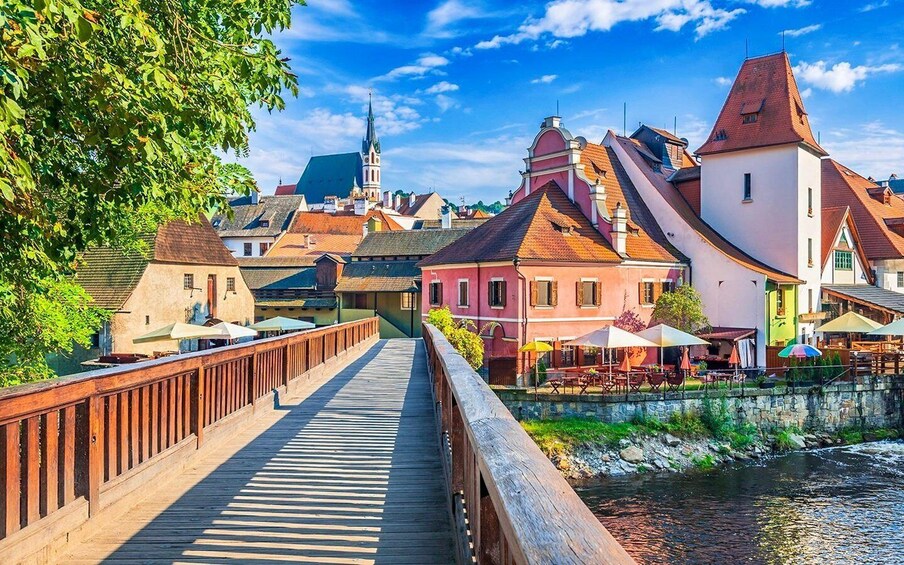 A wooden bridge over a river, colorful buildings, and a church steeple. 2