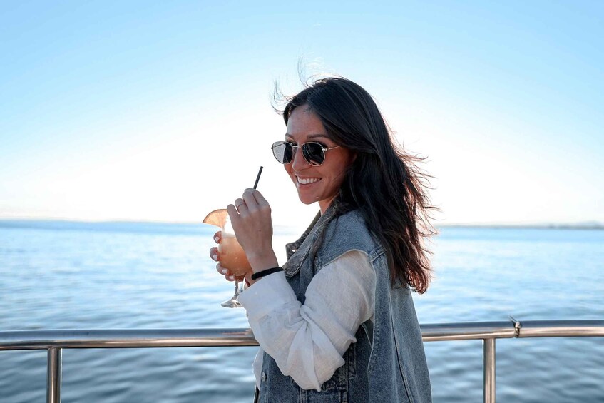 A person holding a drink with a straw, standing on a boat with a view of the water. 1