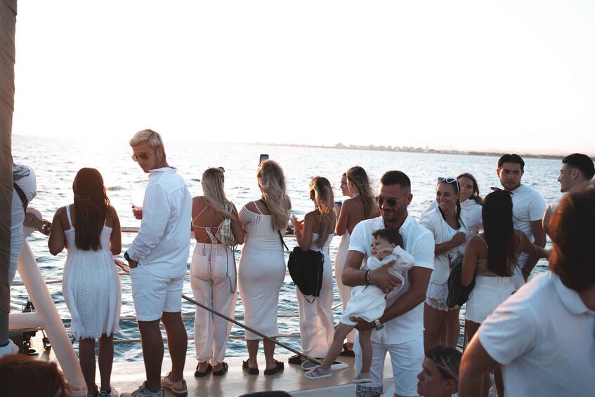 A group of people on a boat, some holding children, with a calm sea and a distant shoreline in the background. 5