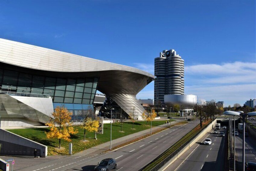 Un edificio moderno con techo curvo, una estructura cilíndrica alta y un cielo azul despejado. 5