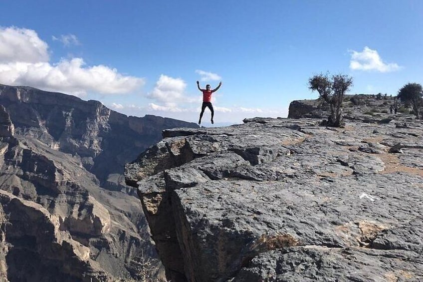 A person standing on a rocky cliff with arms raised, overlooking a canyon. 1