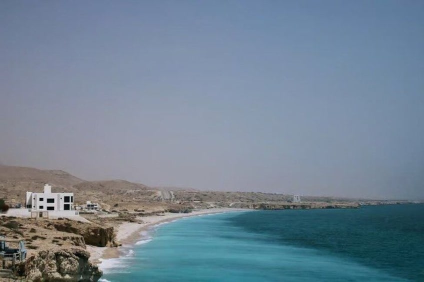 A coastal landscape with a clear sky, a sandy beach, and a few buildings near the shore. 3