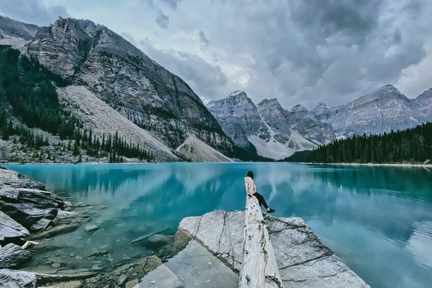 A person sitting on a rock by a turquoise lake surrounded by mountains. 5