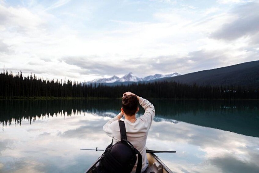 A person in a boat on a calm lake with mountains in the background. 4