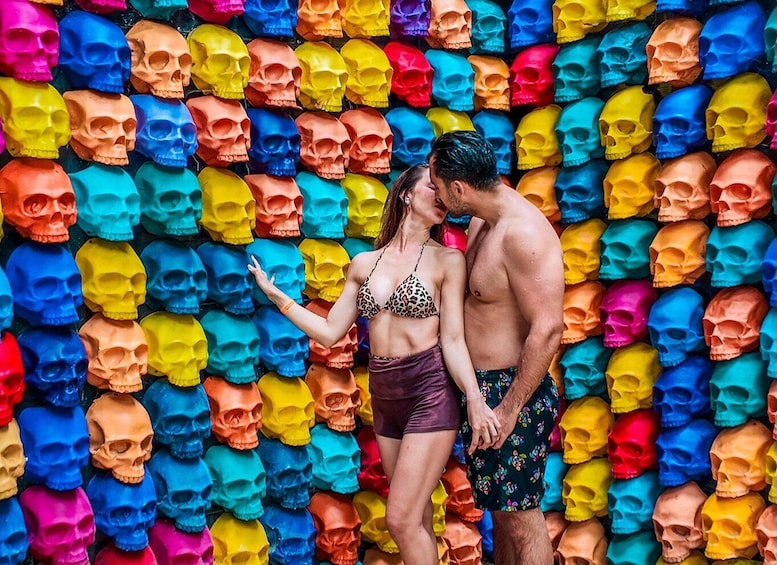 A couple standing in front of a wall of colorful skulls. 1