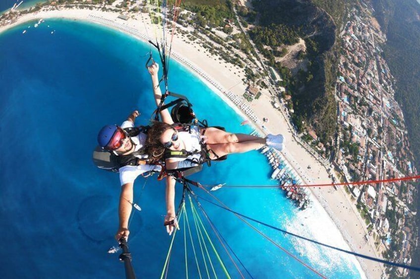 Une personne pratiquant le parapente au-dessus d’une zone côtière, avec une plage et une ville en arrière-plan. 1