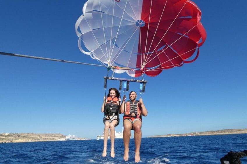 Two people parasailing over the ocean with a clear sky and a distant coastline. 5