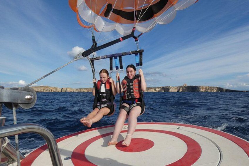 Two people parasailing on a boat with a rocky coastline in the background. 2