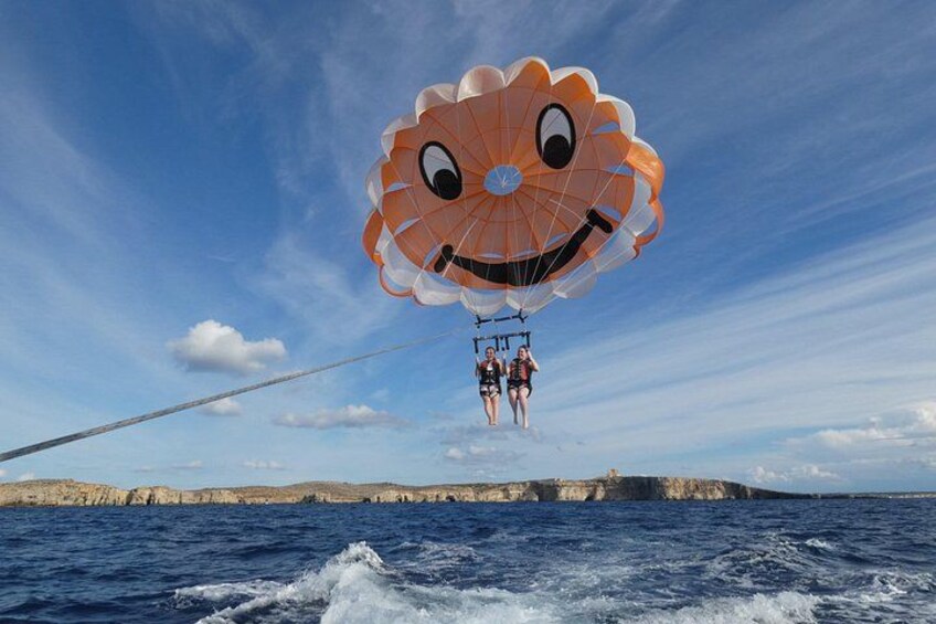 A parasail with a smiling face design over the ocean, with cliffs in the background. 3
