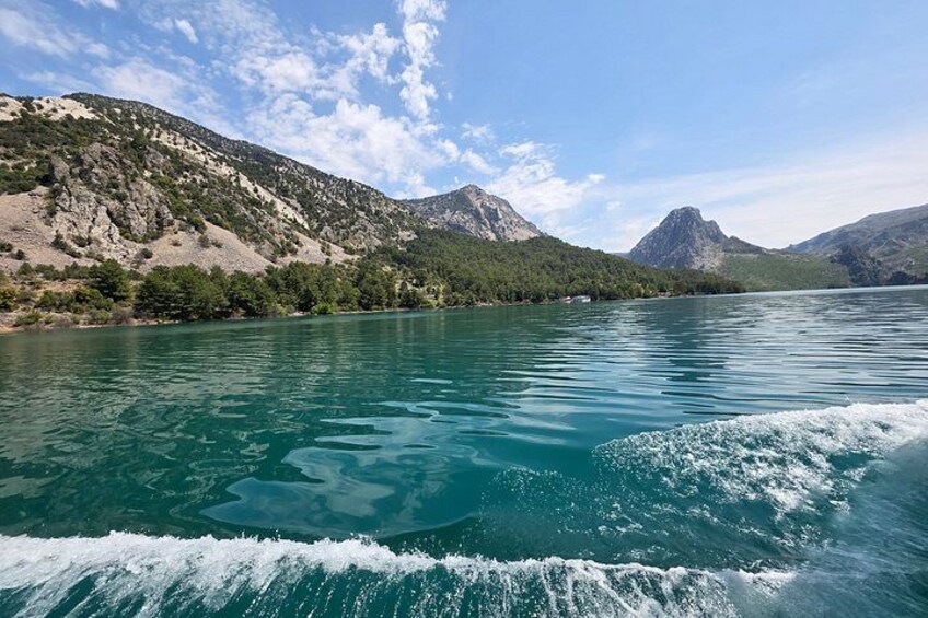 A lake with mountains in the background and a boat creating waves in the foreground. 2
