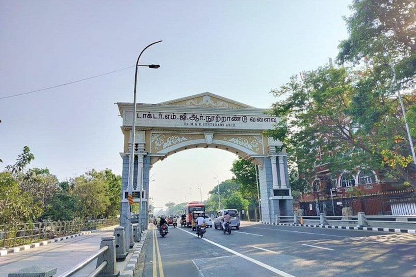 A large archway with text, a road with vehicles, and trees. 5