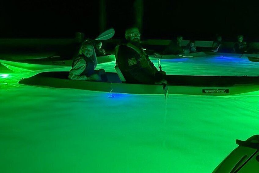A person sitting in a kayak on a green-lit water surface. 5