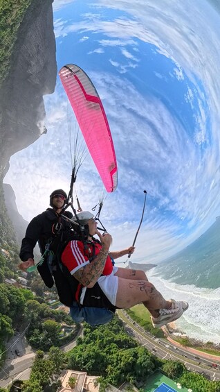 A person paragliding with a pink canopy, overlooking a coastal landscape with cliffs and a road. 1