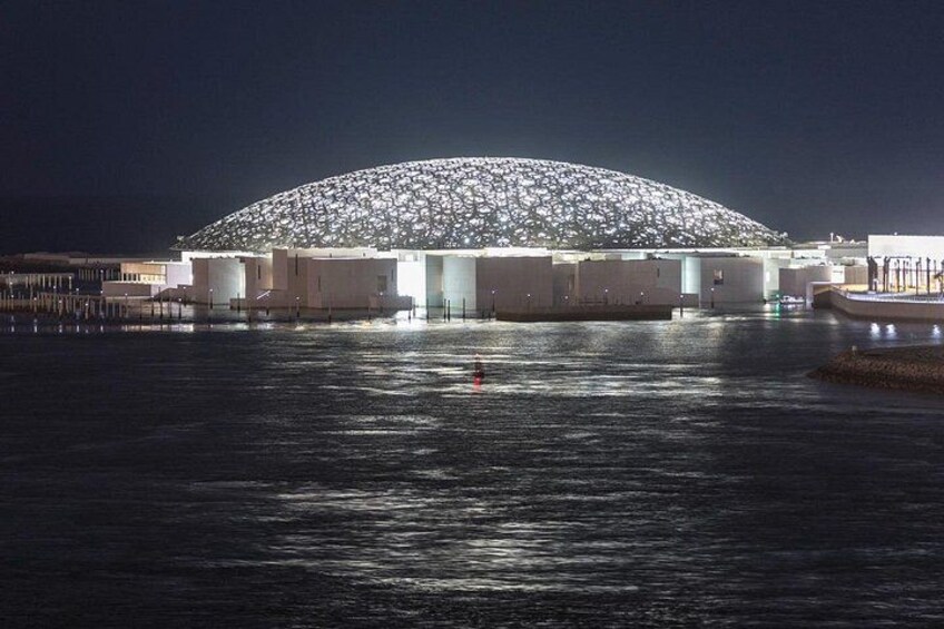 Een grote, verlichte koepelstructuur aan het water in de nacht. 2
