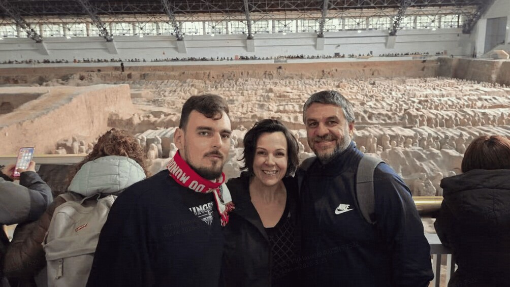 Three people standing in front of a large indoor arena with a crowd of people in the background. 2