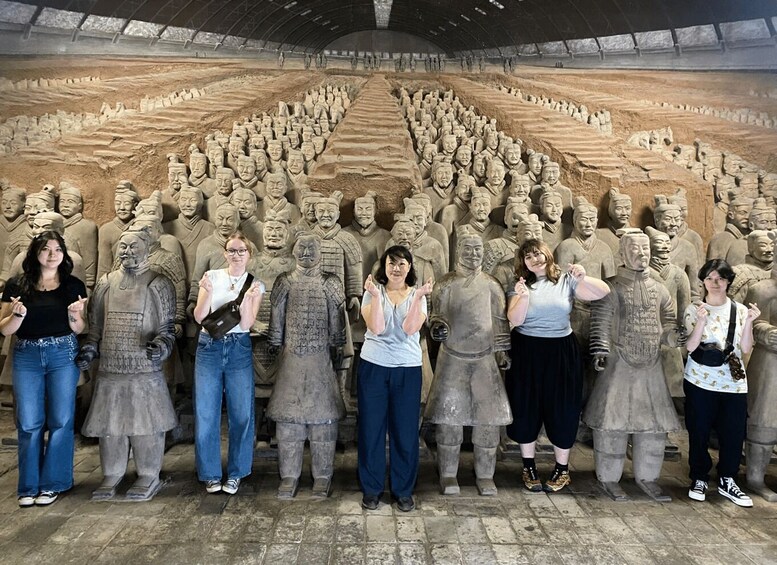 A group of tourists standing in front of a large terracotta army display. 1