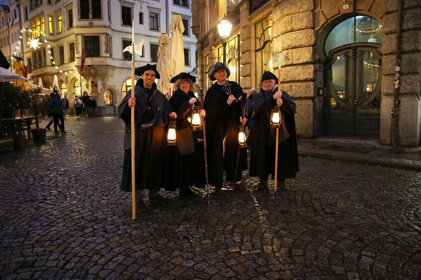 A group of people in historical costumes holding lanterns on a cobblestone street at night. 3