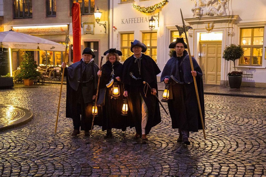 A cobblestone street with a group of people in historical costumes holding lanterns. 2