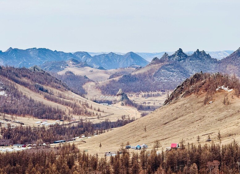 A mountainous landscape with a valley, sparse trees, and a few buildings. 2
