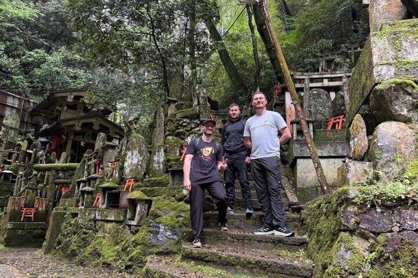 A group of people standing on stone steps in a forested area with moss-covered rocks and traditional Japanese structures. 3