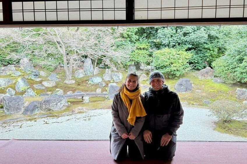 Two people sitting in a traditional Japanese building with a view of a garden with rocks and trees. 4