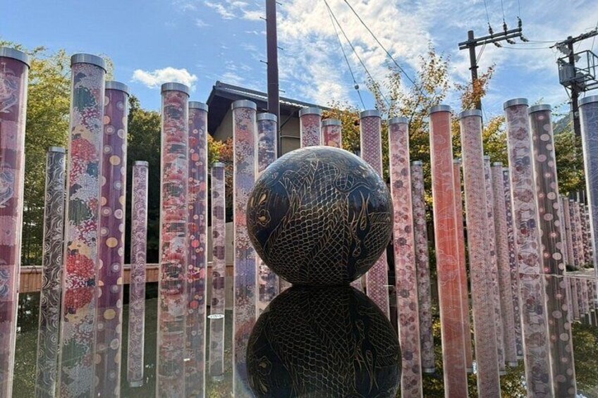 A sculpture of a black sphere with a textured surface, surrounded by vertical panels with painted designs. 2