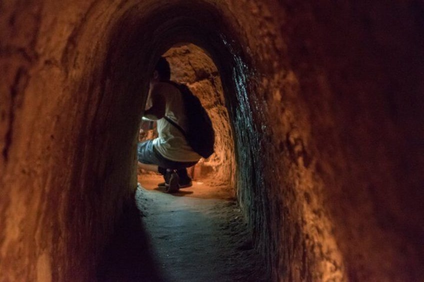 Una persona agachada dentro de un estrecho túnel de piedra abovedado. 3