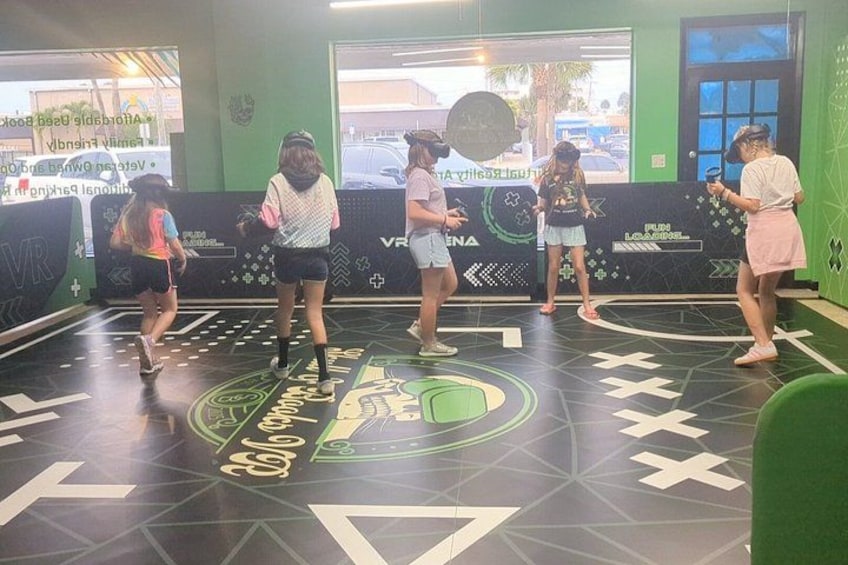 A group of people in a VR gaming area with a green and black floor design. 5