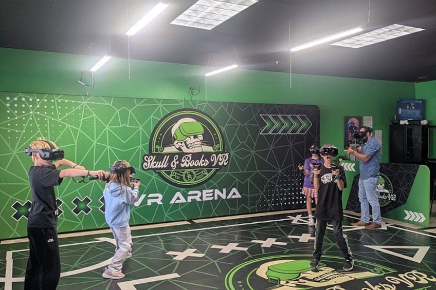 A VR arena with a skull and books logo, green walls, and a geometric floor design. 2