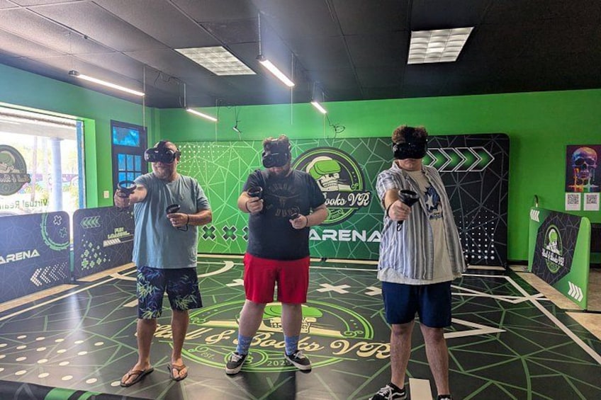 Three people in a VR gaming area with green walls and a geometric floor design. 3