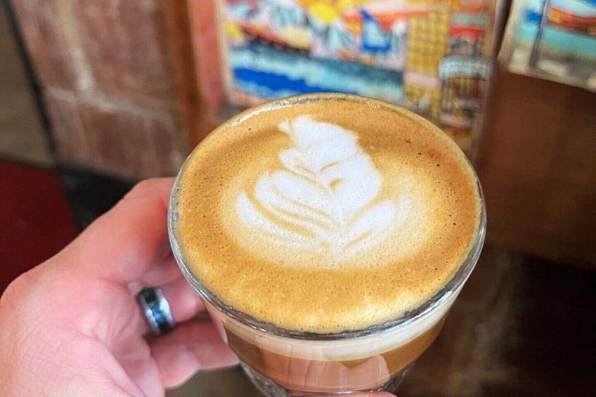 A hand holding a glass of coffee with a latte art design. 1