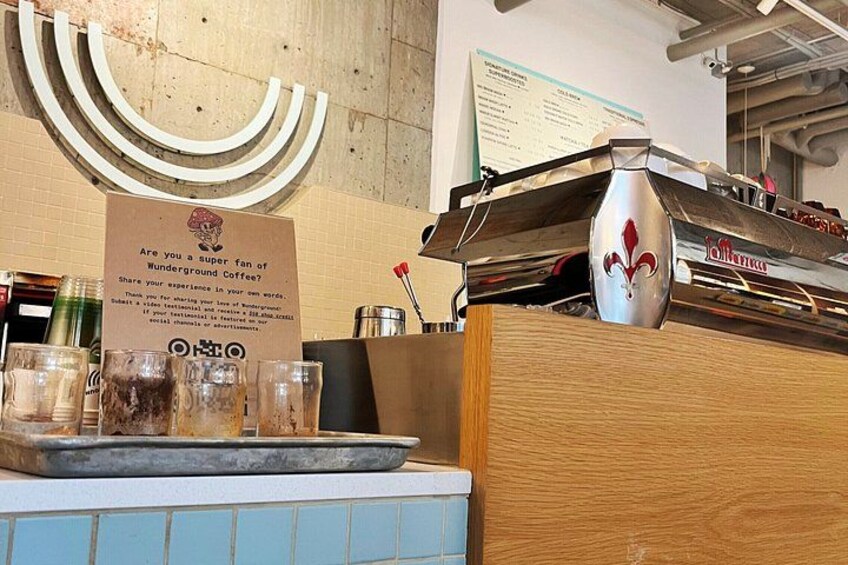 A coffee shop counter with a sign, a coffee machine, and a menu board. 2
