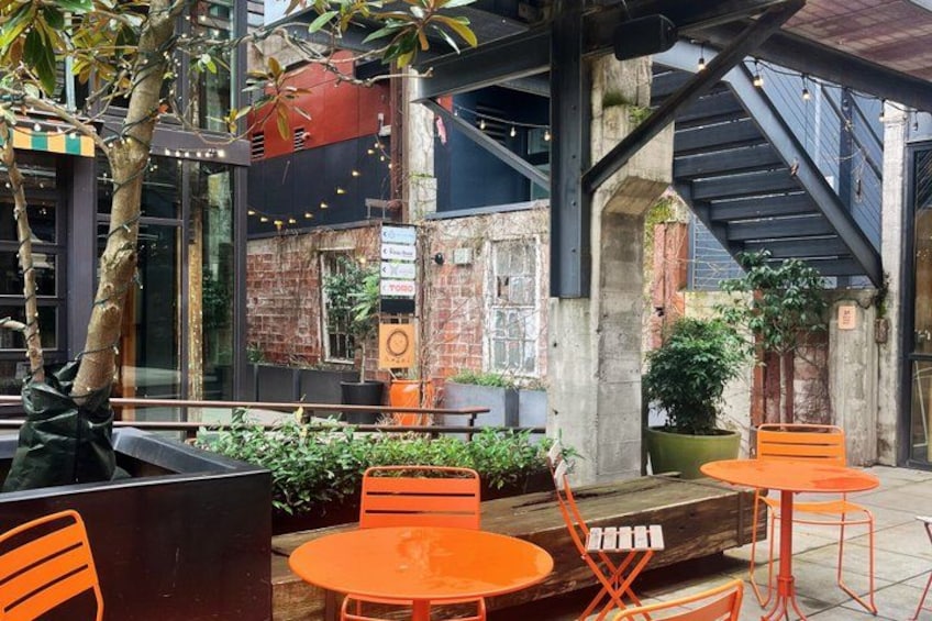 An outdoor seating area with orange chairs and tables, surrounded by plants and a brick wall. 4