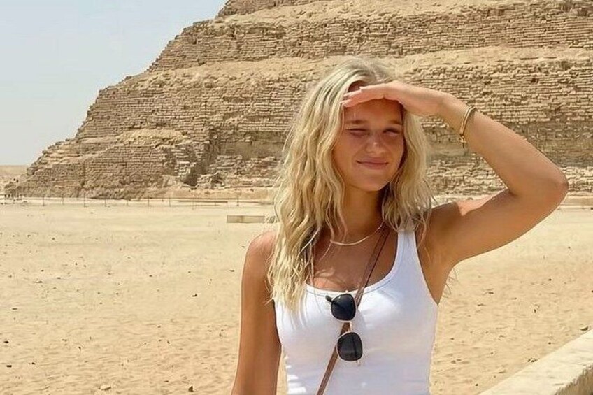 A person standing in a desert with a large pyramid in the background. 4