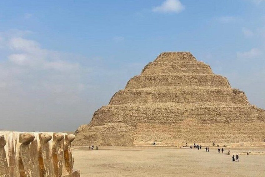 A large pyramid structure with a flat top and a broad base, surrounded by a flat landscape with a few people scattered around. 1