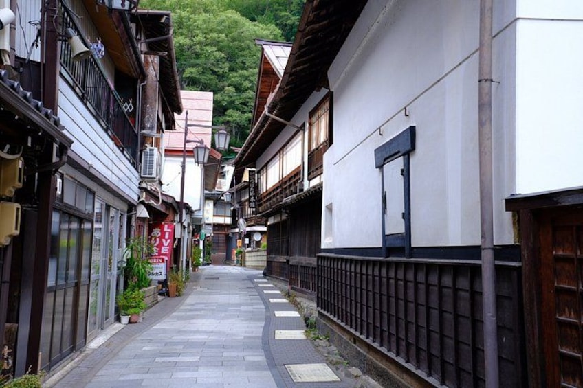 A narrow alleyway with traditional buildings, a wooden fence, and a signboard. 3