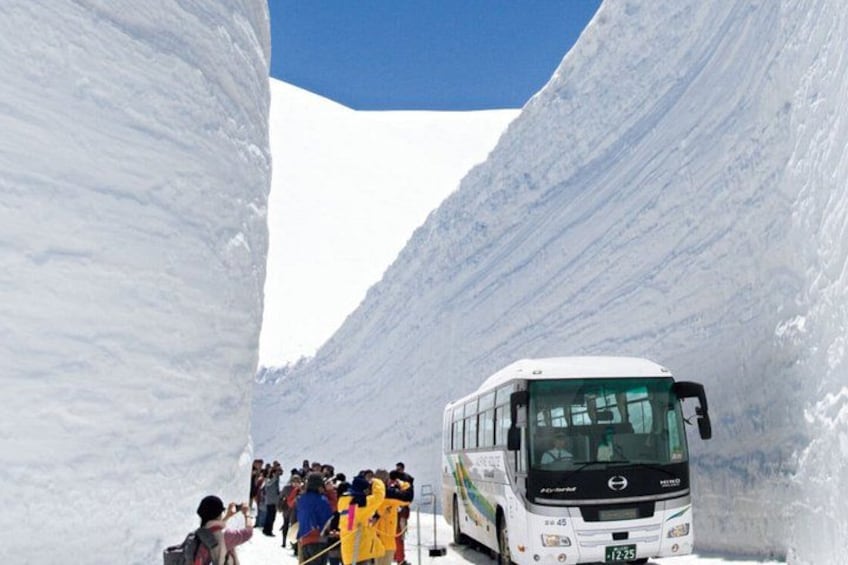 A white bus with passengers at the base of a snow-covered mountain. 2