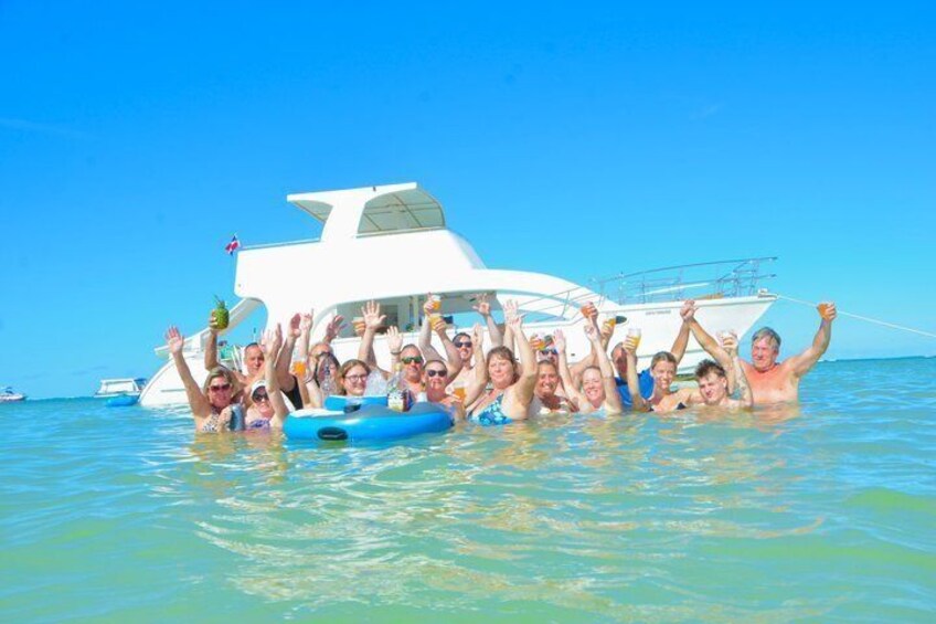 A group of people on a boat in clear blue water, with a white yacht in the background. 1