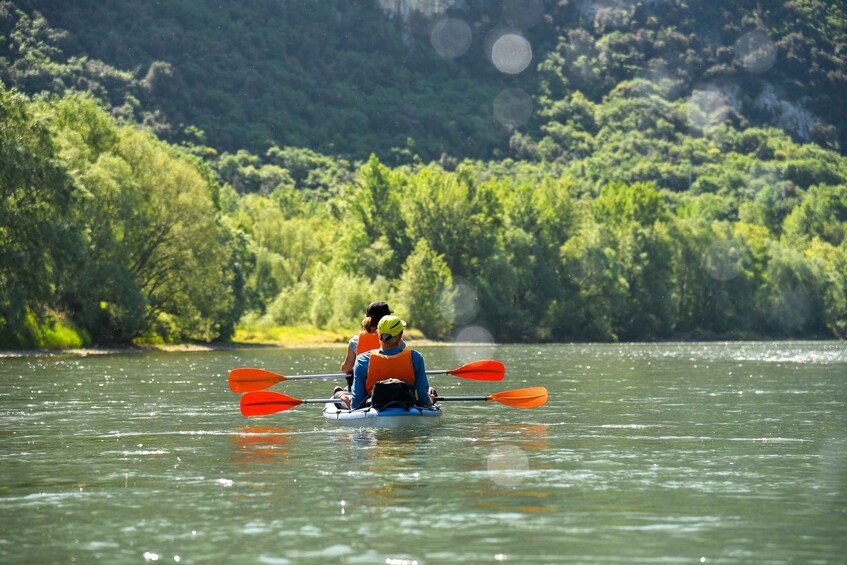 Two people kayaking on a calm river surrounded by lush greenery. 5
